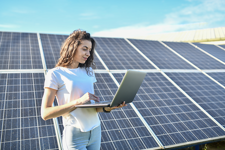 Frau mit Laptop vor Solaranlage